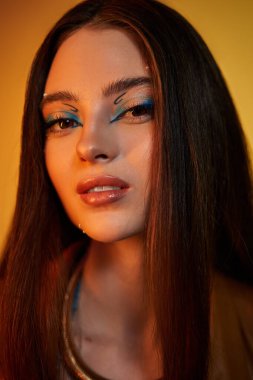 Genç bir kadın, kendine güvenen bir şekilde stüdyoda poz veriyor, modaya uygun yılan baskısı ve kalın makyaj yapıyor..