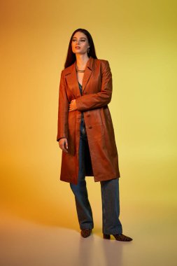 Güzel, genç bir kadın kendine güvenerek şık giysiler içinde parlak bir arkaplanda duruyor..