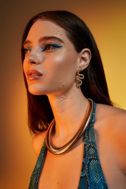 Güzel genç bir kadın zarif poz veriyor, yılan desenli elbisesini ve büyüleyici makyajını sergiliyor..