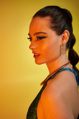 Genç bir kadın, canlı bir yılan desenli moda ve sarı bir zemine karşı cesur makyaj sergiliyor..