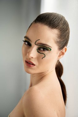 Young woman models striking snake-inspired makeup in a stylish studio, captivating all around. clipart