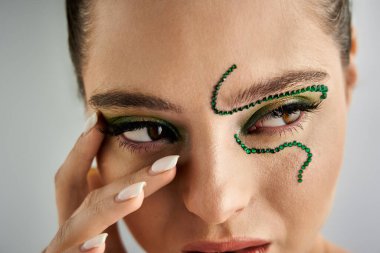 Beautiful young woman showcases striking snake makeup while posing in a fashion studio setting. clipart