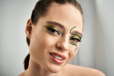 A beautiful young woman poses with striking snake makeup designs and vibrant colors in a studio. clipart