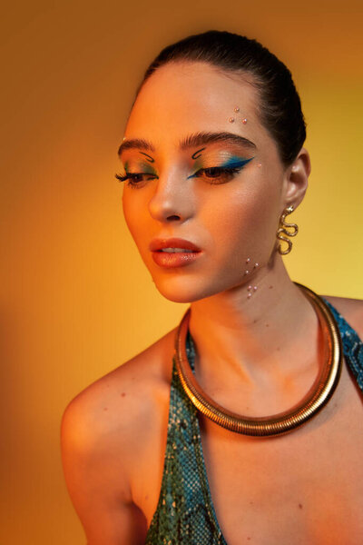 Молодая женщина демонстрирует модные костюмы для печати змей и смелый макияж на теплом фоне.