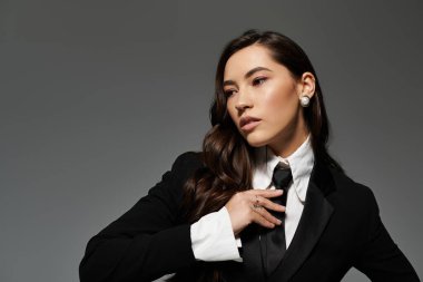 Uzun kahverengi saçlı kendine güvenen genç bir kadın stüdyo ortamında sofistike bir kıyafet sergiliyor..