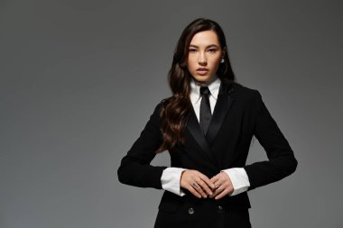 Kendine güvenen genç bir kadın, minimalist gri bir arka plana karşı şık bir şekilde poz verir..