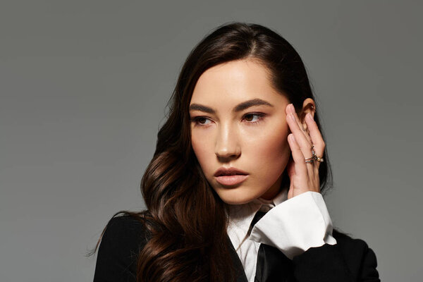 A lovely young woman with long brown hair poses in stylish attire against a grey background.