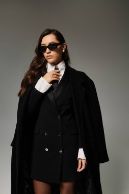 Güzel, genç bir kadın kendine güvenerek poz verir, şık siyah beyaz elbisesiyle zarafet saçar..