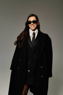 Uzun kahverengi saçlı güzel bir genç kadın şık bir siyah elbisenin içinde rahatça poz veriyor..