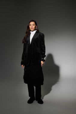 Parlak kahverengi saçlı güzel bir genç kadın zarif bir elbise içinde gri bir arkaplana karşı poz veriyor..