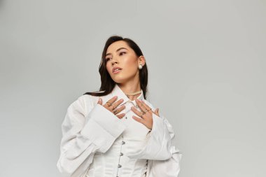 Genç bir kadın şık beyaz bir elbiseyle göz kamaştırıcı aksesuarlarla zarafet sergiliyor..