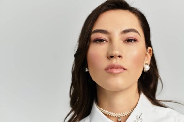 Genç ve güzel bir kadın şık tarzını sergiliyor ve sade bir arka plana karşı duruyor..