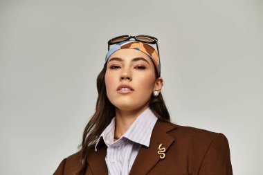 A beautiful young woman exudes confidence wearing a chic brown blazer and a patterned headscarf. clipart