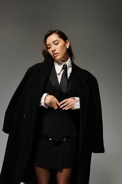 Изящная молодая женщина в шикарном черно-белом одеянии излучает уверенность в минималистской студии.