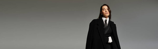 Confident young woman with long brown hair poses elegantly against a grey backdrop, banner