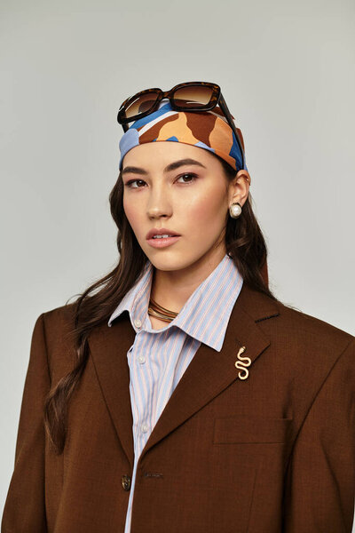 Стильная молодая женщина уверенно позирует в шикарном коричневом пиджаке и ярком платке.