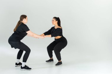 İki güçlü kadın kooperatif bir çömelme egzersizi yapıyor, takım çalışması ve spor yapıyor..