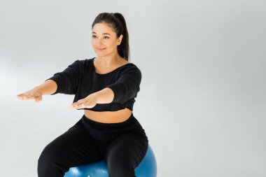 Spor giyim sektöründe bir kadın, parlak bir alanda egzersiz yaparken mavi bir egzersiz topunun üzerinde dengede durur..