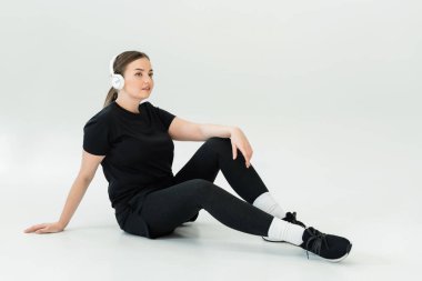 Güçlü ve güzel bir kadın yerde oturuyor, spor kıyafetleri ve kulaklıklar takıyor, ara veriyor..