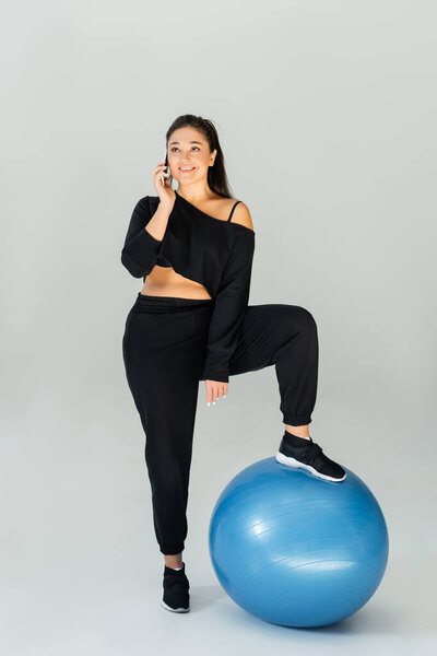 Сильная и здоровая женщина уверенно балансирует на синем шаре упражнений, болтая по телефону.