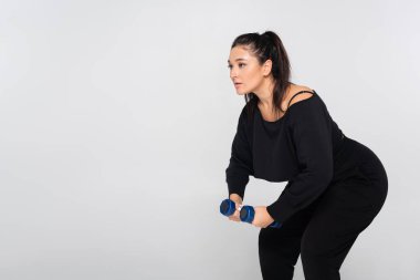 Spor kıyafetleri içinde formda bir kadın, halterli iç mekan kuvveti antrenmanı yapıyor..