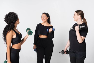 Üç güçlü kadın ağırlık kaldırırken spor ipuçlarını paylaşıyor, destekleyici bir topluluk kuruyor.