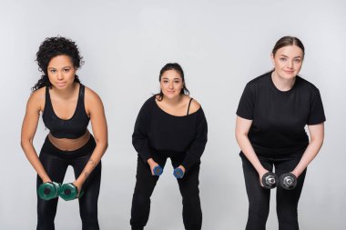 Üç kararlı kadın modern bir stüdyoda halter kaldırıyor, güç ve spor yapıyor..