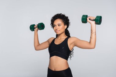 Formda bir kadın ağırlık kaldırma egzersizini iki dambılla yaparken fitness hedeflerine odaklanır..