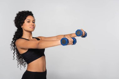 Formda bir kadın iyi aydınlatılmış, modern bir spor salonunda dambıllarla güç antrenmanı yapar..