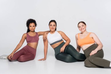 Üç kendine güvenen kadın, bir stüdyoda modaya uygun spor kıyafetlerinde güç ve zindelik gösteriyor..