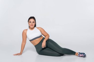 Dişi fitness modeli düz bir arkaplan karşısında trend egzersiz ekipmanında güvenle poz verir.