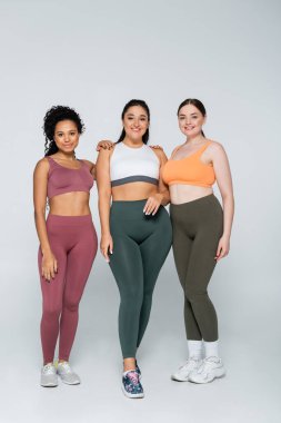 Üç kendine güvenen kadın şık fitness kıyafetleri içinde birlikte durur, gücü ve güzelliği kutlarlar..