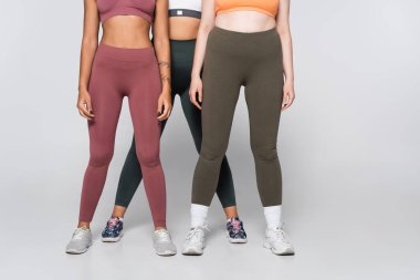 Üç zinde kadın renkli spor kıyafetleriyle poz veriyor, spor yaparken özgüven ve atletizmi somutlaştırıyor..