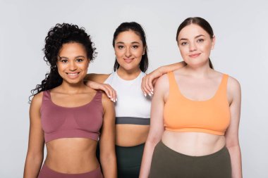 Üç güçlü ve formda kadın renkli spor kıyafetlerini giyerken gururla atletizmlerini sergilerler..