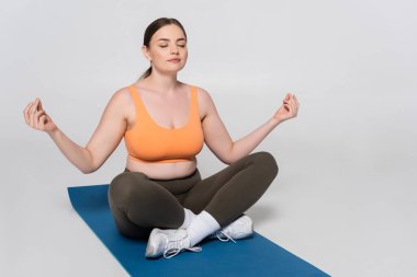 Formda bir dişi, mavi bir hasırda huzur içinde meditasyon yapıyor. Spor kıyafetleriyle sükunetini kucaklıyor..