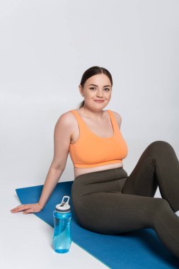 Formda bir kadın, güçlü bir egzersizden sonra yoga minderinde dinlenir. Güç ve güzellik saçar..