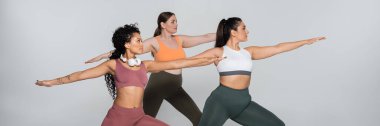 Üç kararlı kadın yoga pozisyonunda, renkli spor kıyafetlerinde güç ve güzellik sergiliyorlar..