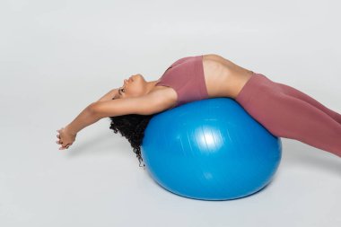 Bir bayan sporcu modern bir fitness stüdyosunda mavi bir denge topu üzerinde esneme egzersizi yapıyor..