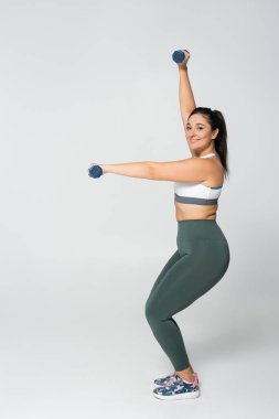 Şık spor elbiseli kadın dambılları kaldırıyor, parlak ortamlarda güç ve zindelik gösteriyor..