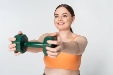 Formda bir kadın, modern bir spor salonunda halterlerle egzersiz yaparken gülümser..