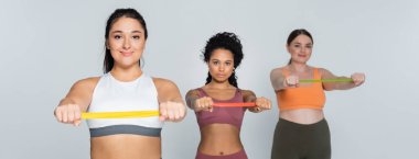 Three determined female athletes focus on strengthening their bodies with resistance bands. clipart