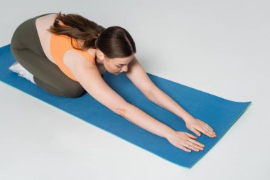 Kendini işine adamış bir kadın mavi yoga minderinde derin bir gerinme yaşar..