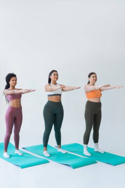 Üç güçlü kadın, iyi aydınlatılmış bir stüdyoda canlı paspaslar üzerinde senkronize fitness pozu pratiği yapıyor..