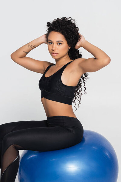 Сильная и здоровая женщина уверенно позирует на голубом шаре стабильности, прославляя атлетику и красоту.