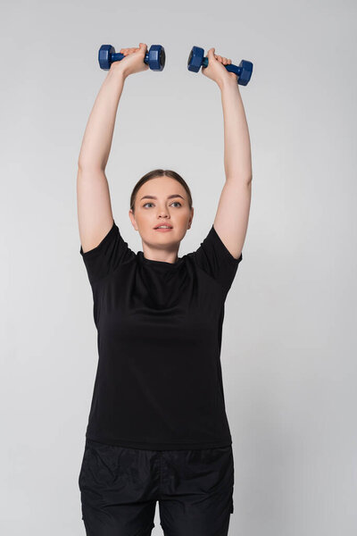 Женщина демонстрирует силу и решимость, поднимая гантели во время тренировки