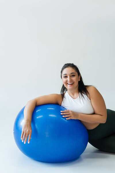 Фигуристка позирует с синим мячом для упражнений в яркой студии во время тренировки.