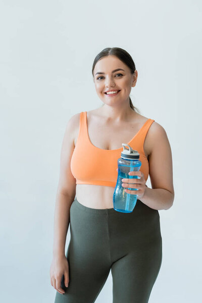 A fit woman poses confidently with a blue water bottle, ready for her workout.