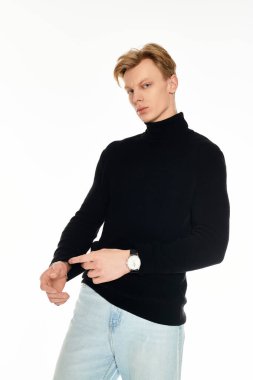 Genç bir adam siyah kazak ve mavi kot pantolon içinde şık bir poz verir..