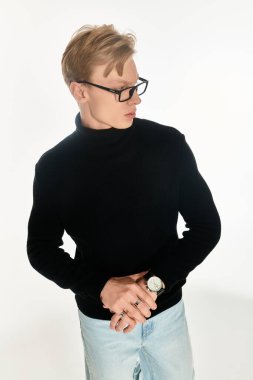 Gözlüklü genç adam kendinden emin duruyor, modern bir stil ve zarif bir saat sergiliyor..