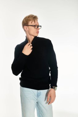 A young man stands tall in a black sweater, adjusting his collar with a confident gaze. clipart